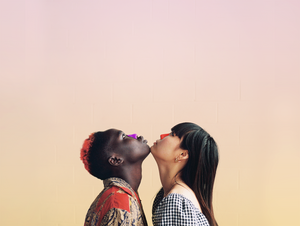 A man with red and black hair and a woman with black hair as well as orange and purple sunscreen on their nose's while they look up and their chins touch